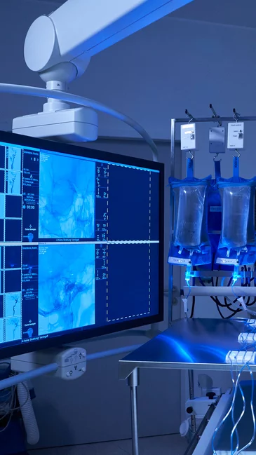 Foto: Gesco: Operationssaal mit medizinischen Geraeten, darunter ein Monitor mit mehreren Anzeigen, ein Infusionsgestell mit mehreren Fluessigkeitsbeuteln und eine medizinische Beleuchtungsanlage