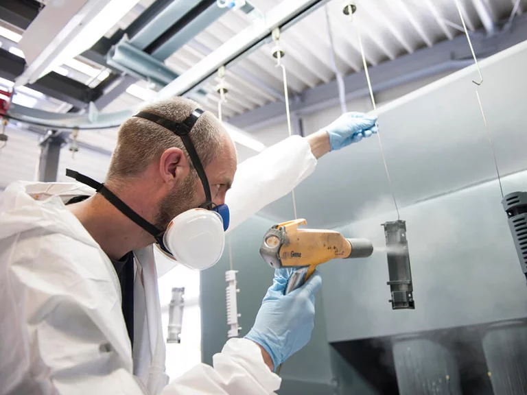 Foto: Gesco: Ein Mann in Schutzkleidung und Maske bearbeitet eine Maschine mit einem Foehn in einer Fabrik