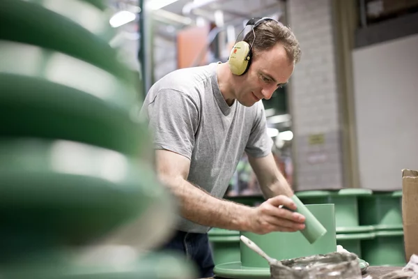 Foto: Gesco: Ein konzentrierter Mann mit Gehörschutz bearbeitet in einer Werkstatt grüne Werkstücke