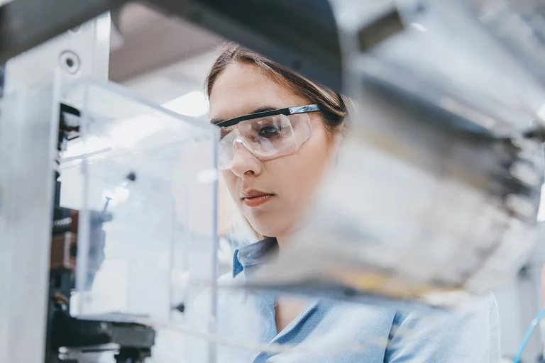 Foto: Gesco: Nahaufnahme einer Frau mit Schutzbrille, sie arbeitet konzentriert an einer Maschine