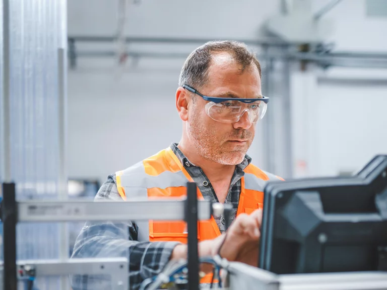 Foto: Gesco: Ein Mann in Schutzbrille und Warnweste, der an einer Maschine in einer Fabrik arbeitet