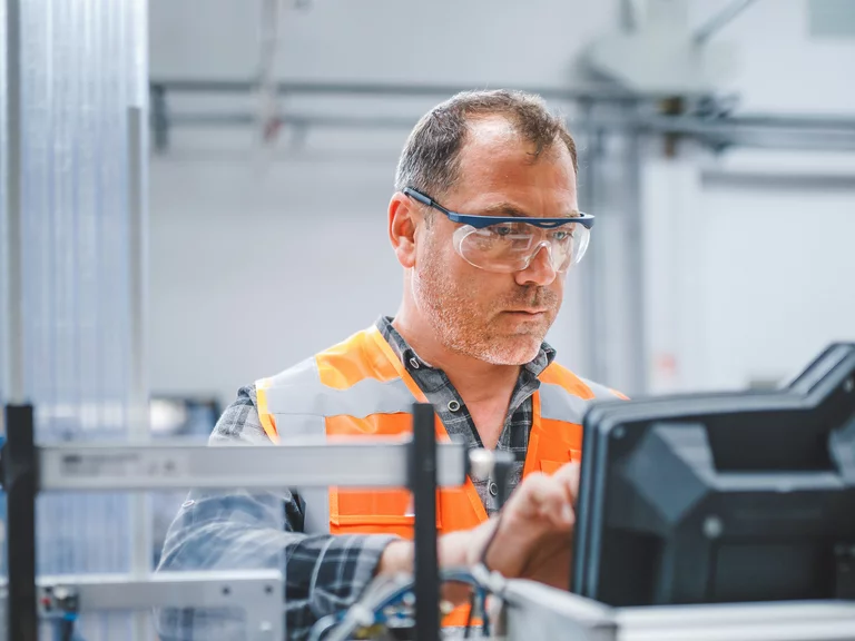 Foto: Gesco: Ein Mann in Schutzbrille und Warnweste, der an einer Maschine in einer Fabrik arbeitet