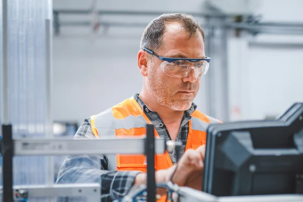 Foto: Gesco: Ein Mann in Schutzbrille und Warnweste, der an einer Maschine in einer Fabrik arbeitet