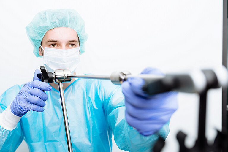 Foto: Gesco: Ein Mann in medizinischer Schutzkleidung und Schutzmaske haelt ein medizinisches Instrument vor sich