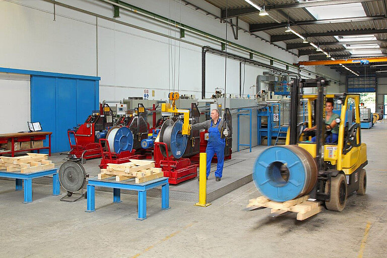 Foto: Gesco: Eine Lagerhalle von Innen, grosse Spulen liegen auf roten Metallgestellen, ein Gabelstapler faehrt rechts
